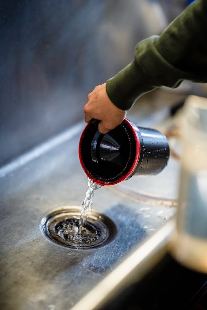 Hand pours water from canister into sink, showcasing daily chores indoors.